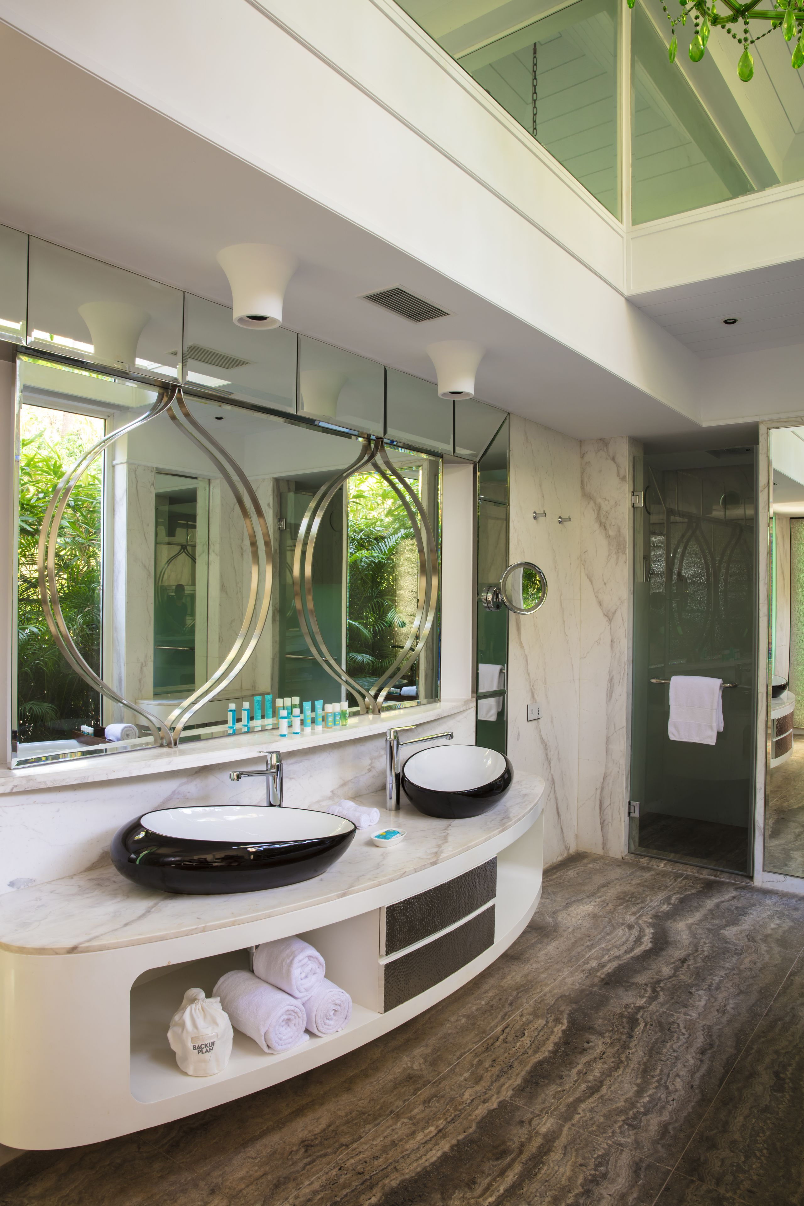 A modern bathroom with a large mirror, two sinks, and a glass shower enclosure.