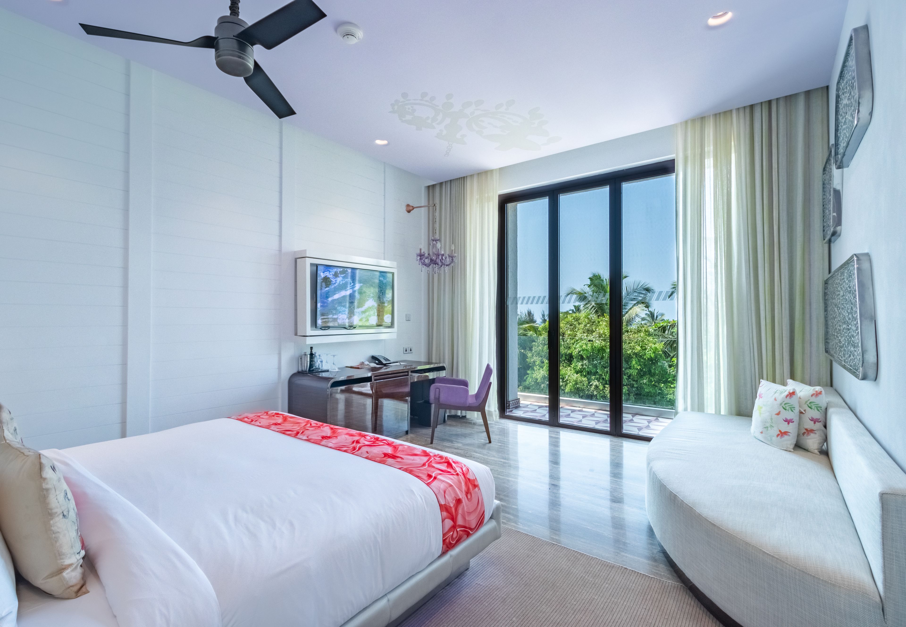 Une chambre d’hôtel moderne équipée d’un lit, d’un bureau, d’un canapé et d’une grande fenêtre donnant sur un paysage verdoyant.