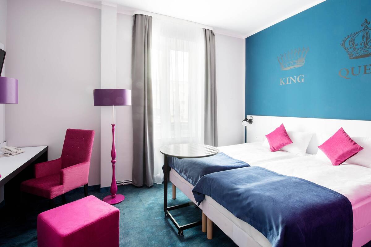 A hotel room with a bed, a desk, a chair, a lamp, and a round table.