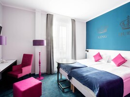 Quarto de hotel com cama, escrivaninha, cadeira, abajur e mesa redonda.