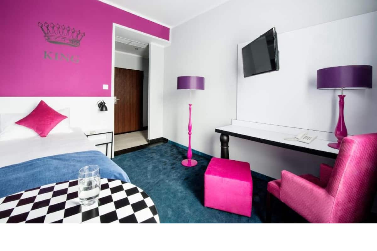 A hotel room with a bed, a desk, a chair, a TV, and a bathroom door.