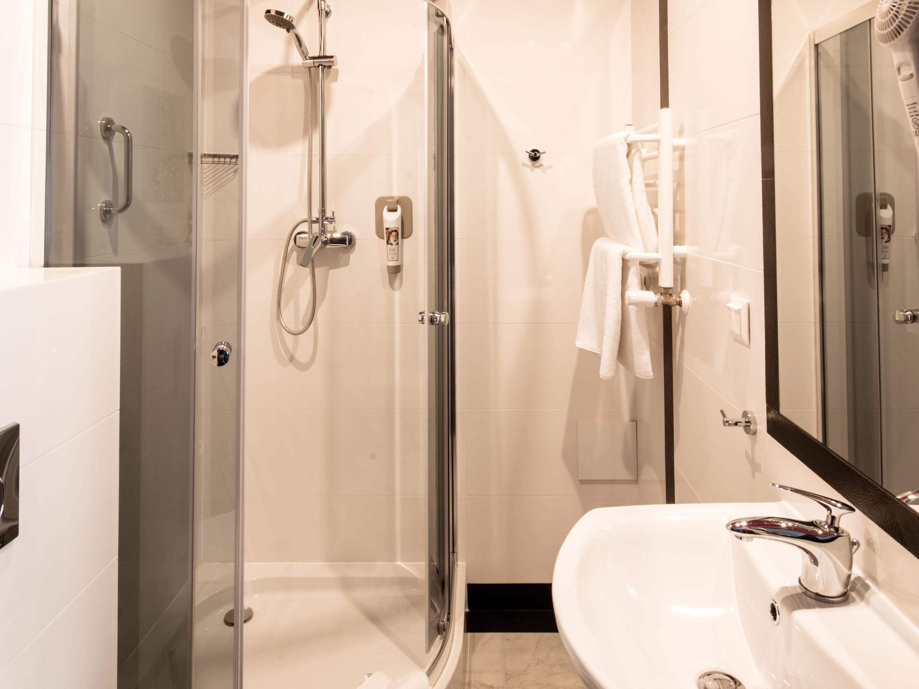 Un baño moderno con ducha de vidrio, lavabo blanco y un espejo grande.