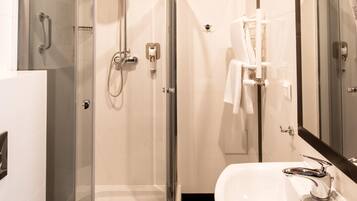 Un baño moderno con ducha de vidrio, lavabo blanco y un espejo grande.