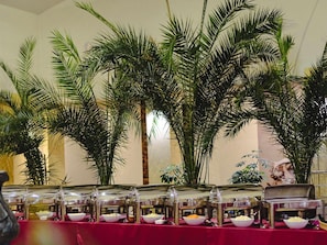 A buffet setup with multiple food stations, surrounded by tall palm trees. - ibis Styles Gniezno Stare Miasto (Gniezno)