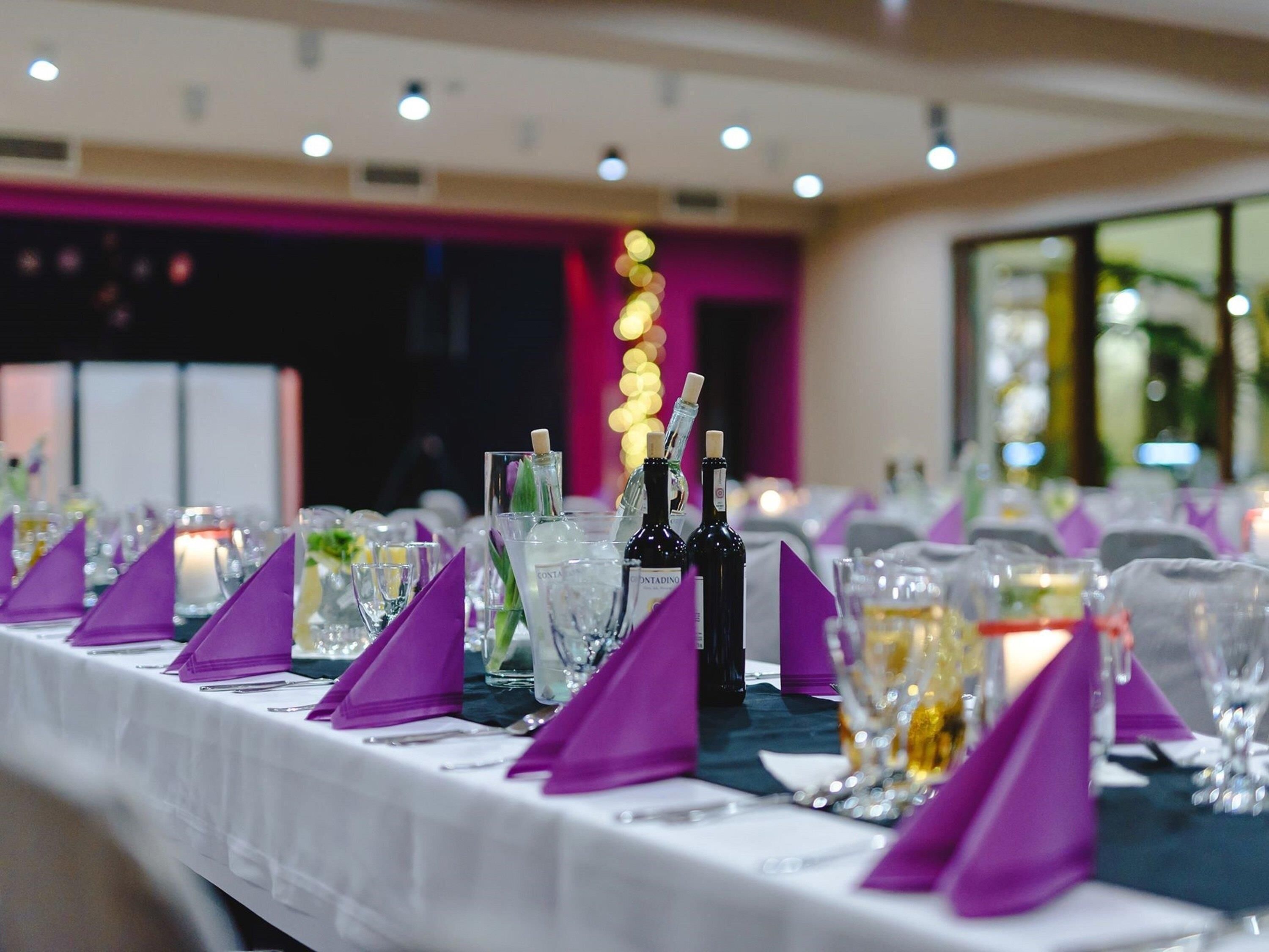A banquet table with purple napkins, clear glasses, and bottles of wine.