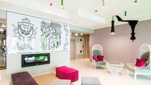 A modern lobby with a large wall mural, seating areas, and a television screen. - ibis Styles Gniezno Stare Miasto (Gniezno)