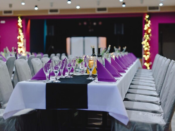 Una larga mesa de banquete con manteles blancos, servilletas moradas y vasos transparentes.