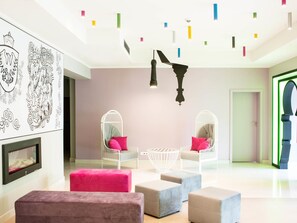 Ein modernes Interieur mit weißer Decke, Wandkunst, einem Kamin und einer Sitzecke mit Poufs und Sesseln.