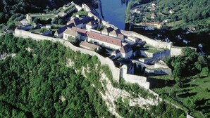 Vista aérea de un pueblo amurallado con un castillo central, rodeado de muros y vegetación.