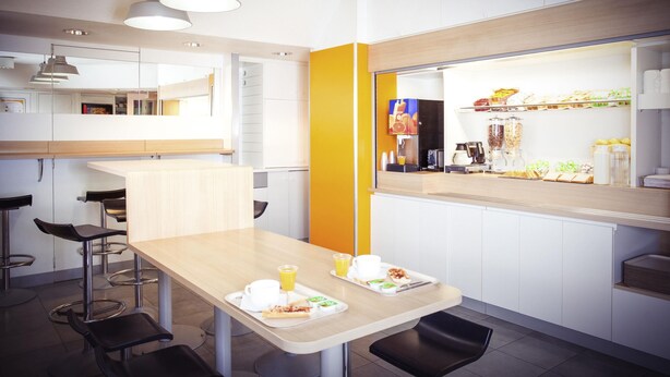 Un café moderno con una mesa de madera, sillas negras y una pared de color amarillo brillante.