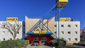 Un hotel con una entrada distintiva en azul y rojo, cielo despejado y un estacionamiento.