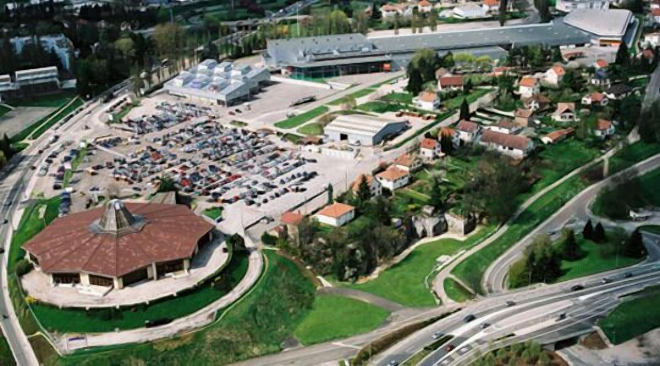 Luchtbeeld van een complex met meerdere gebouwen, een ruime parkeerplaats en omliggend groen.