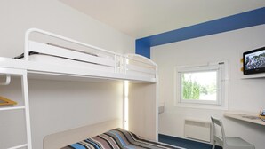 Una cama literera con colcha a rayas, un escritorio con silla, una ventana y un radiador.