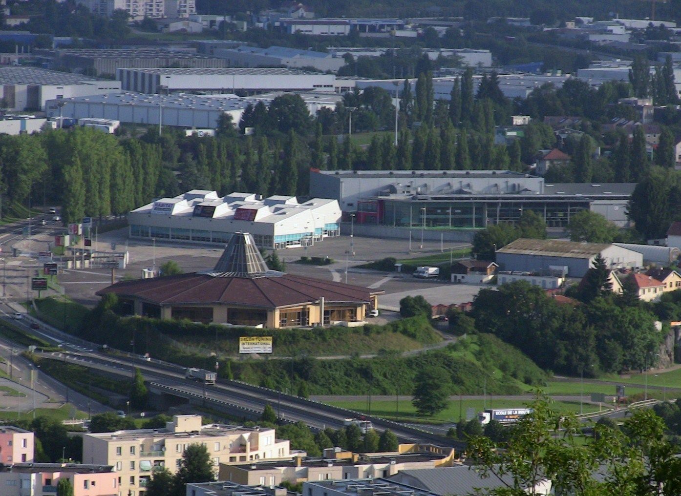 Un'area commerciale con un grande edificio, una struttura più piccola con tetto a punta e un'autostrada a più corsie.