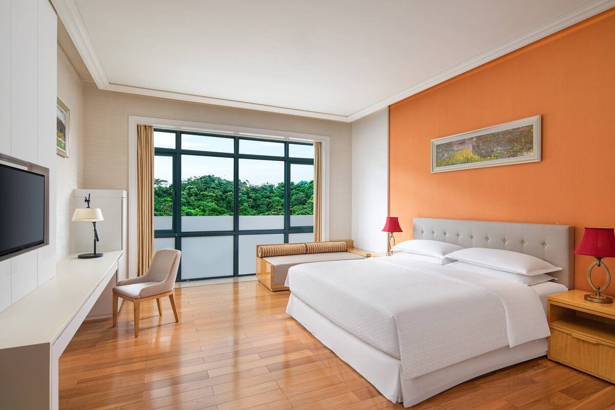 A hotel room with a large bed, a desk, a chair, and a TV.