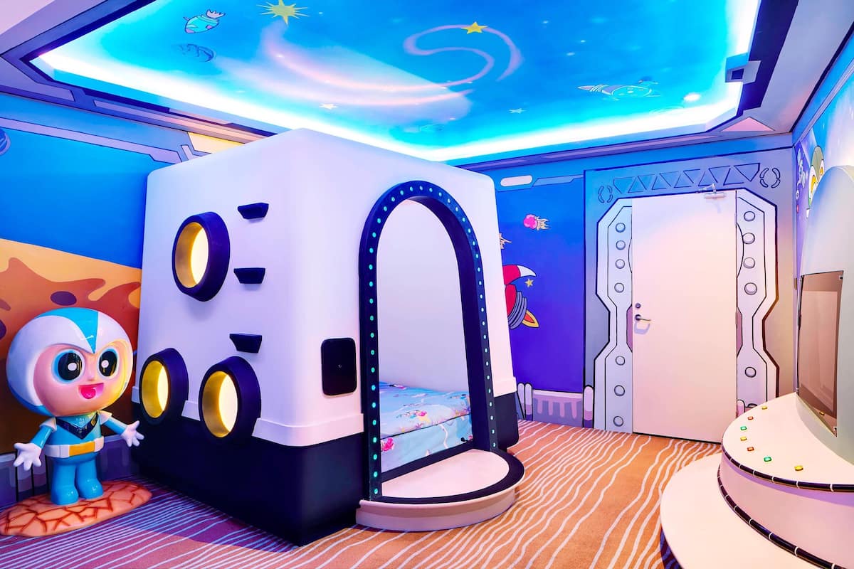 A children's play area with a bed, a toy figure, and a ceiling with a starry design.