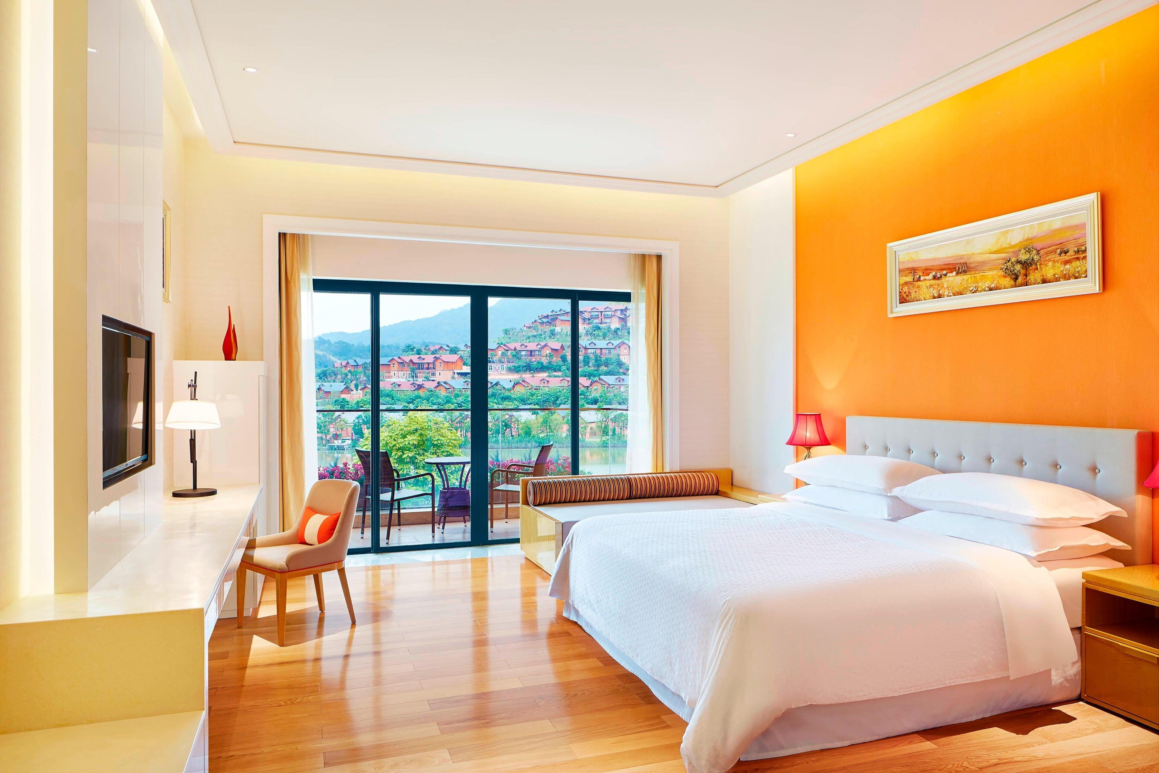 A hotel room with a large bed, a desk, a chair, and a view of a mountainous landscape through a large window.