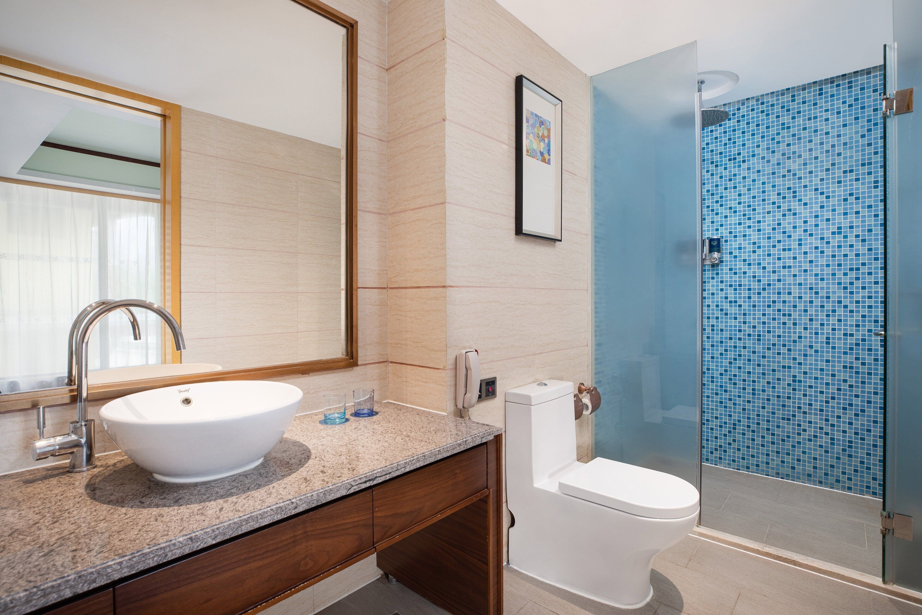 A bathroom with a white sink, a mirror, a toilet, and a glass-enclosed shower with blue mosaic tiles.