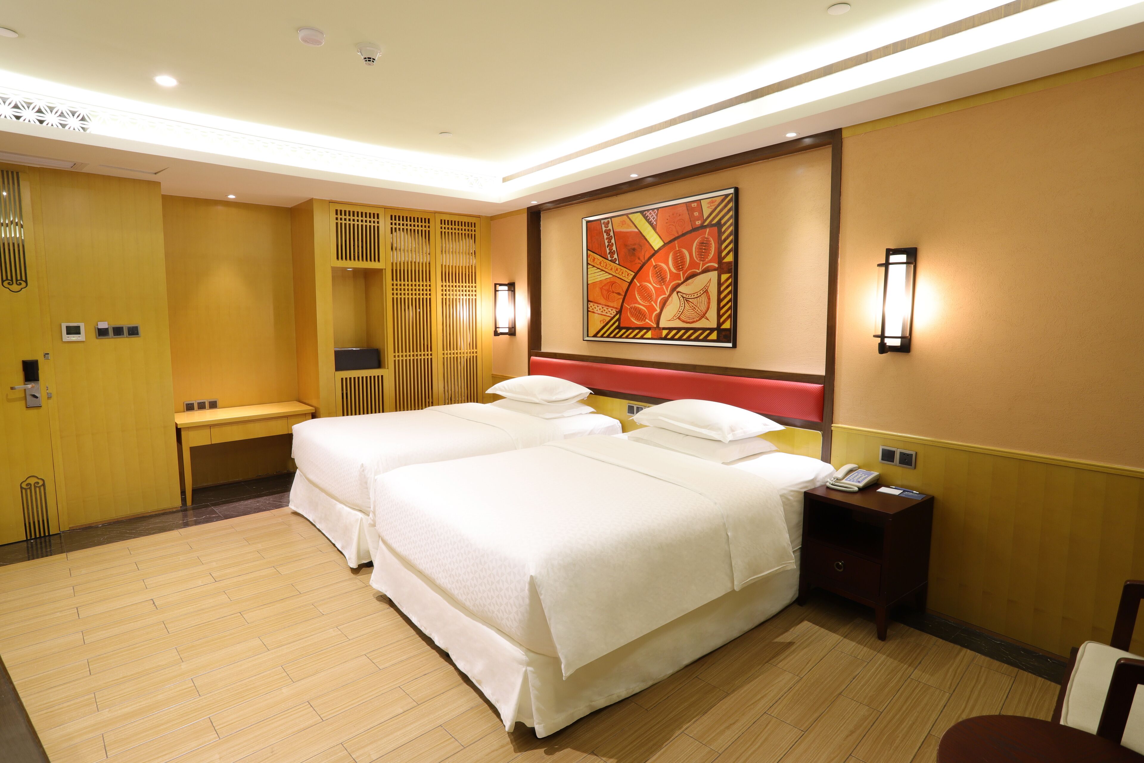 A hotel room with two beds, a desk, a chair, a nightstand, and a wall-mounted artwork.