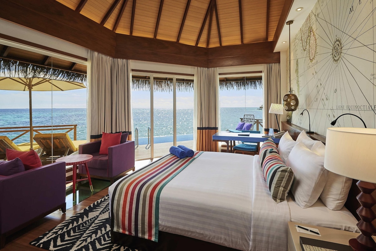 A hotel room with a large bed, a desk, a chair, and a view of the ocean.