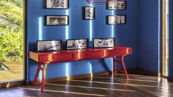 Una stanza con pavimento in legno, una scrivania rossa con cassetti e un muro blu con quadri appesi.