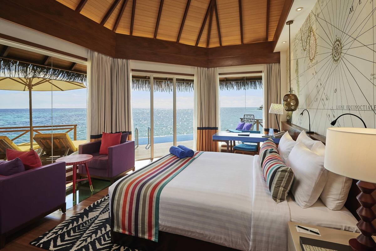 Habitación de hotel con una cama grande, un escritorio, una silla y vista al océano.