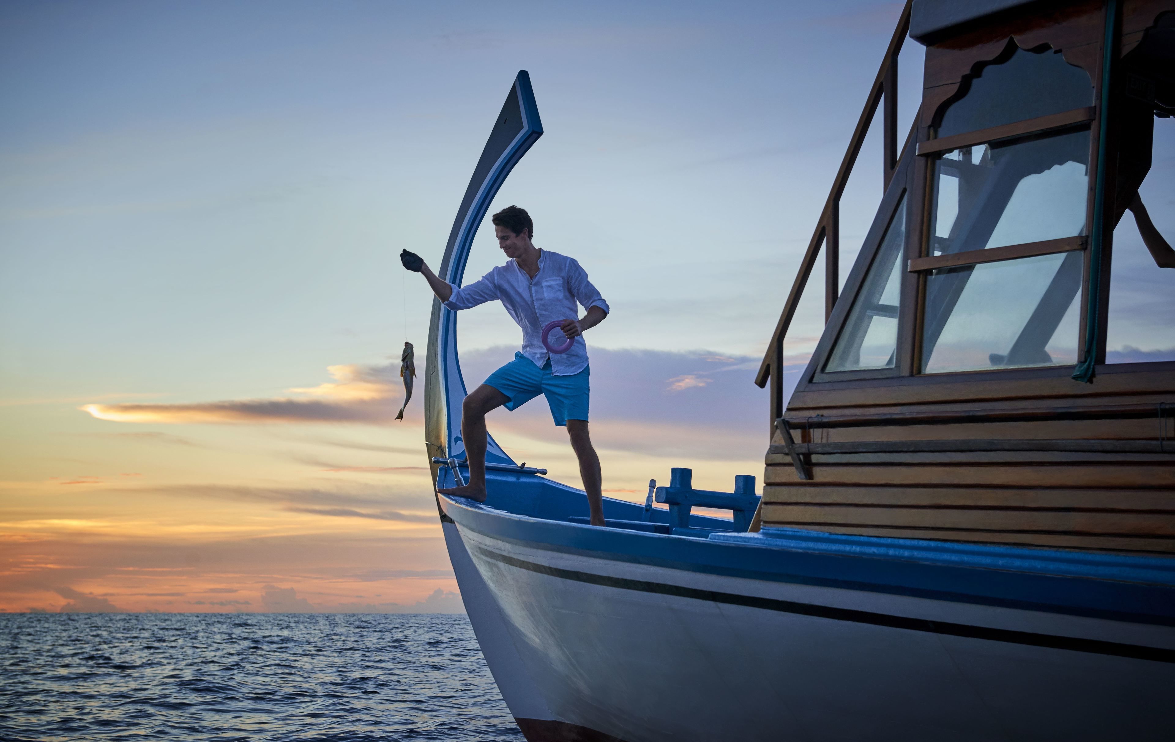 A person standing on a boat with an open door, a view of the sea, and a sunset in the background.