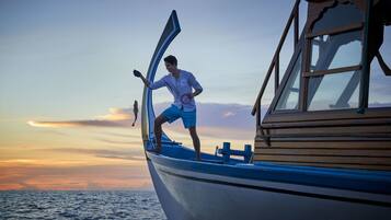 A person standing on a boat with an open door, a view of the sea, and a sunset in the background.