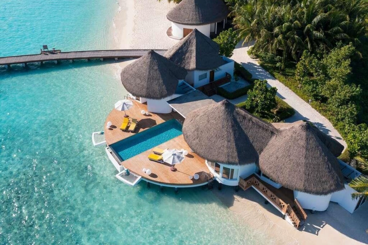 An overwater bungalow with thatched roofs, a pool, and a beach view.