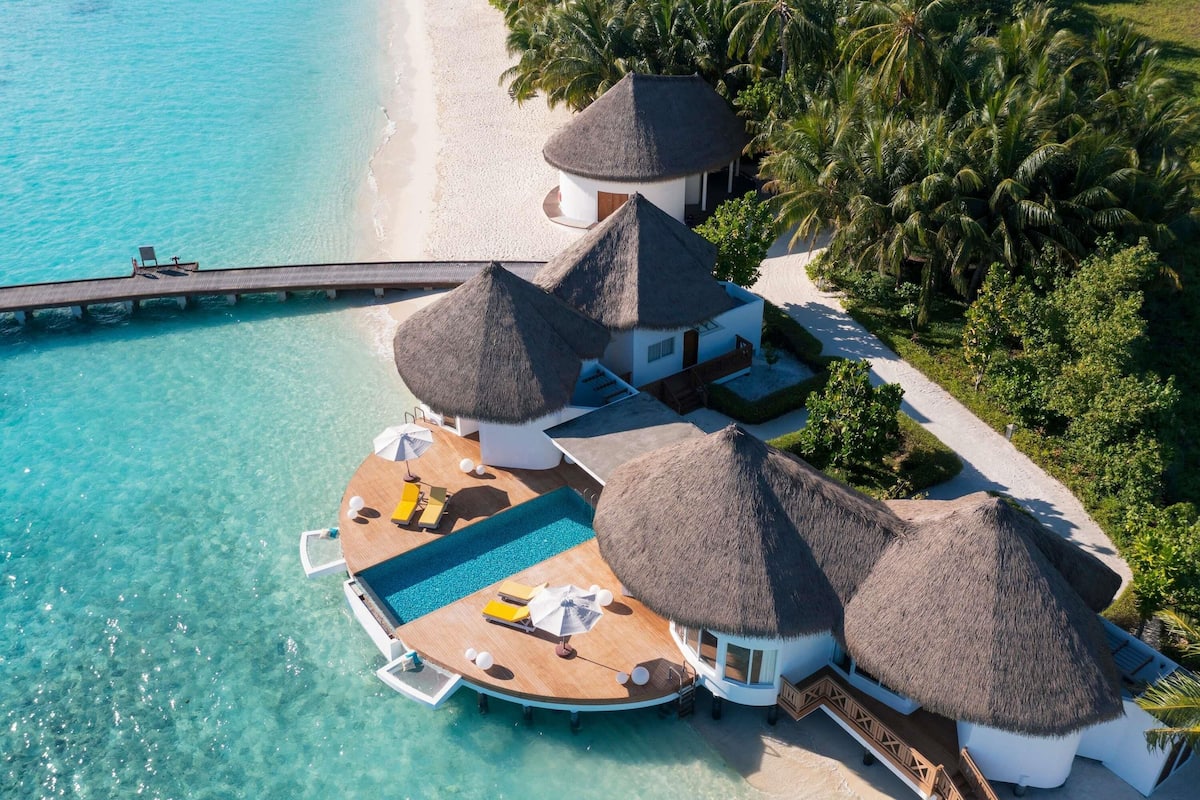 Un bungalow sur pilotis avec piscine, des constructions à toits de chaume et vue sur la plage.