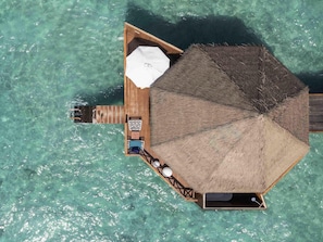 Un bungalow sur pilotis doté d’un toit de chaume, d’une petite terrasse et d’un espace détente avec une table et des chaises.