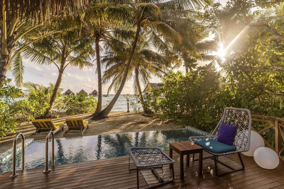 Une terrasse en bois avec une piscine, des chaises longues et une vue sur l’océan et les palmiers.