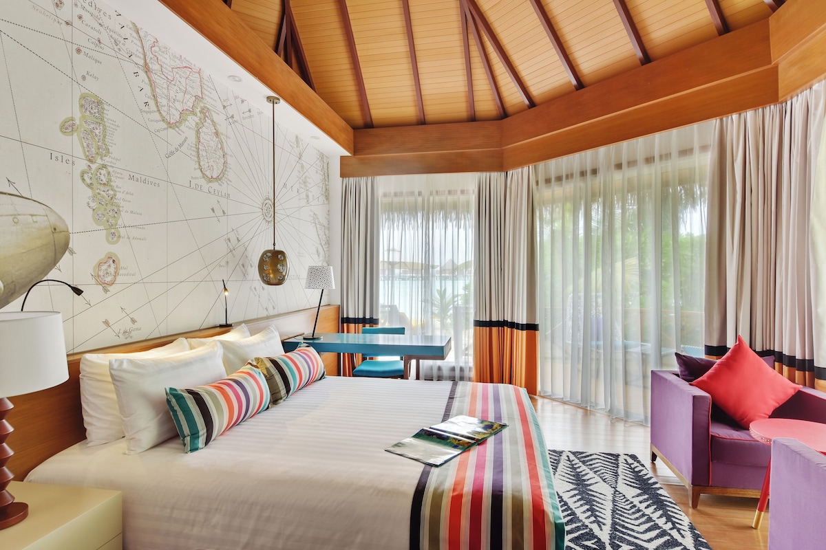 A hotel room with a large bed, a desk, a chair, and a map on the wall.