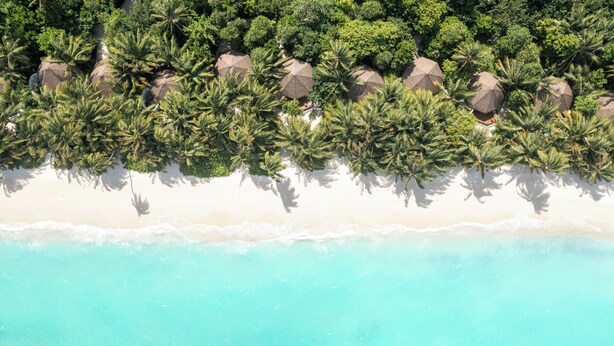 An aerial view of a beach with white sand and turquoise water, surrounded by dense green foliage and large rocks. - Mercure Maldives Kooddoo Adult-Only Resort (Kooddoo)