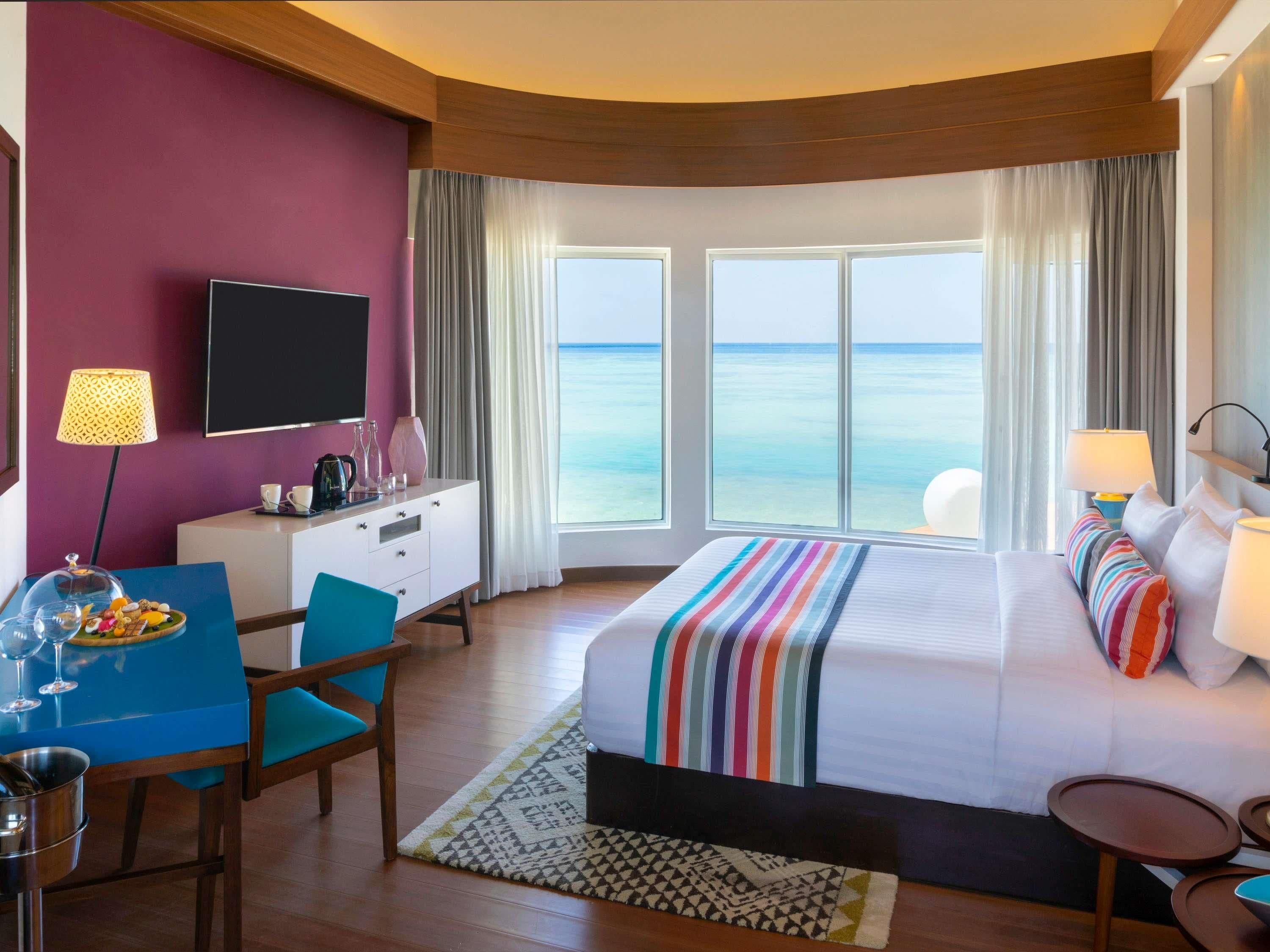 A hotel room with a bed, a desk, a chair, a TV, and a view of the ocean.