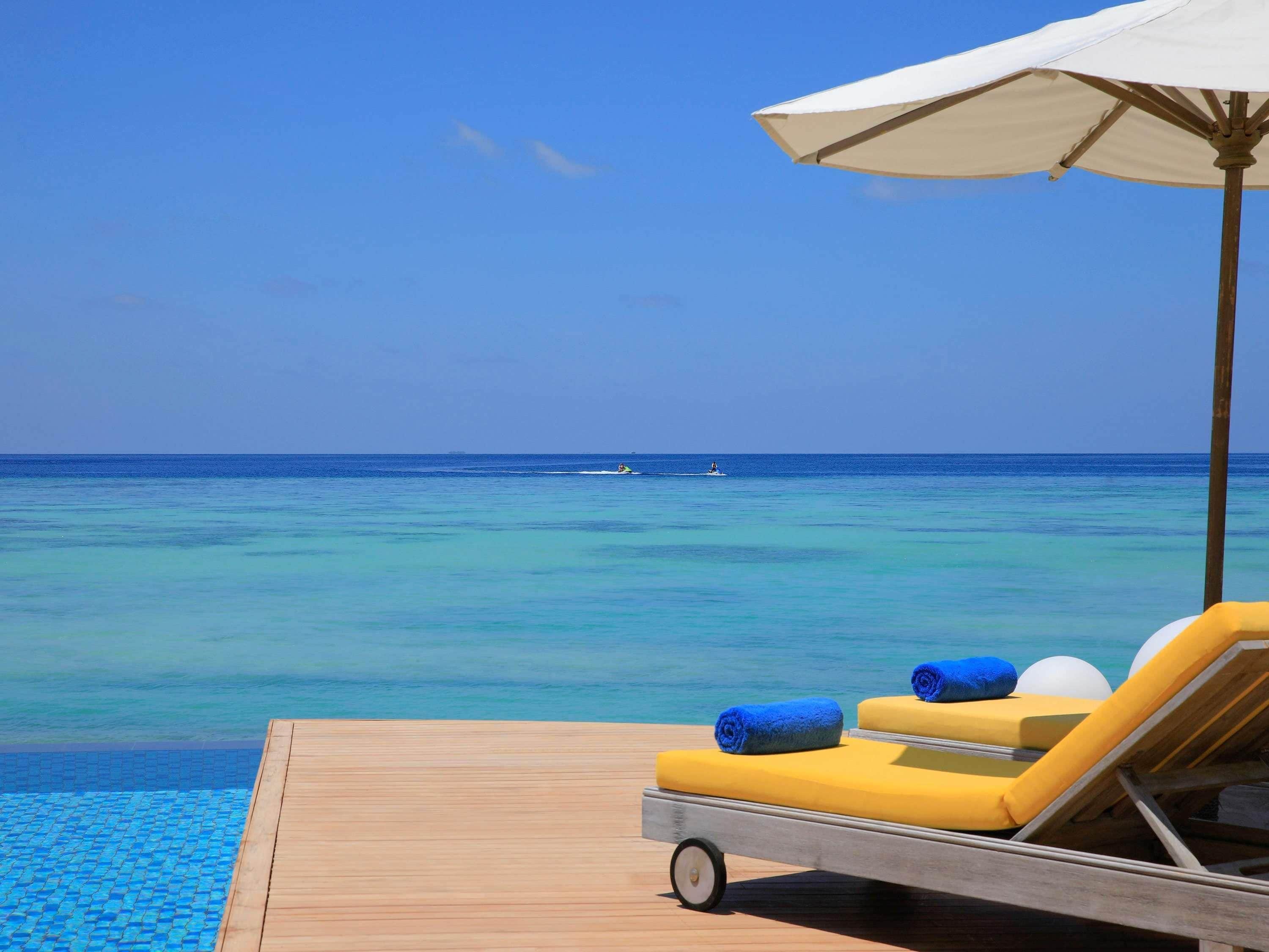 Een houten terras met een ligstoel en parasol, met uitzicht op een heldere blauwe zee.
