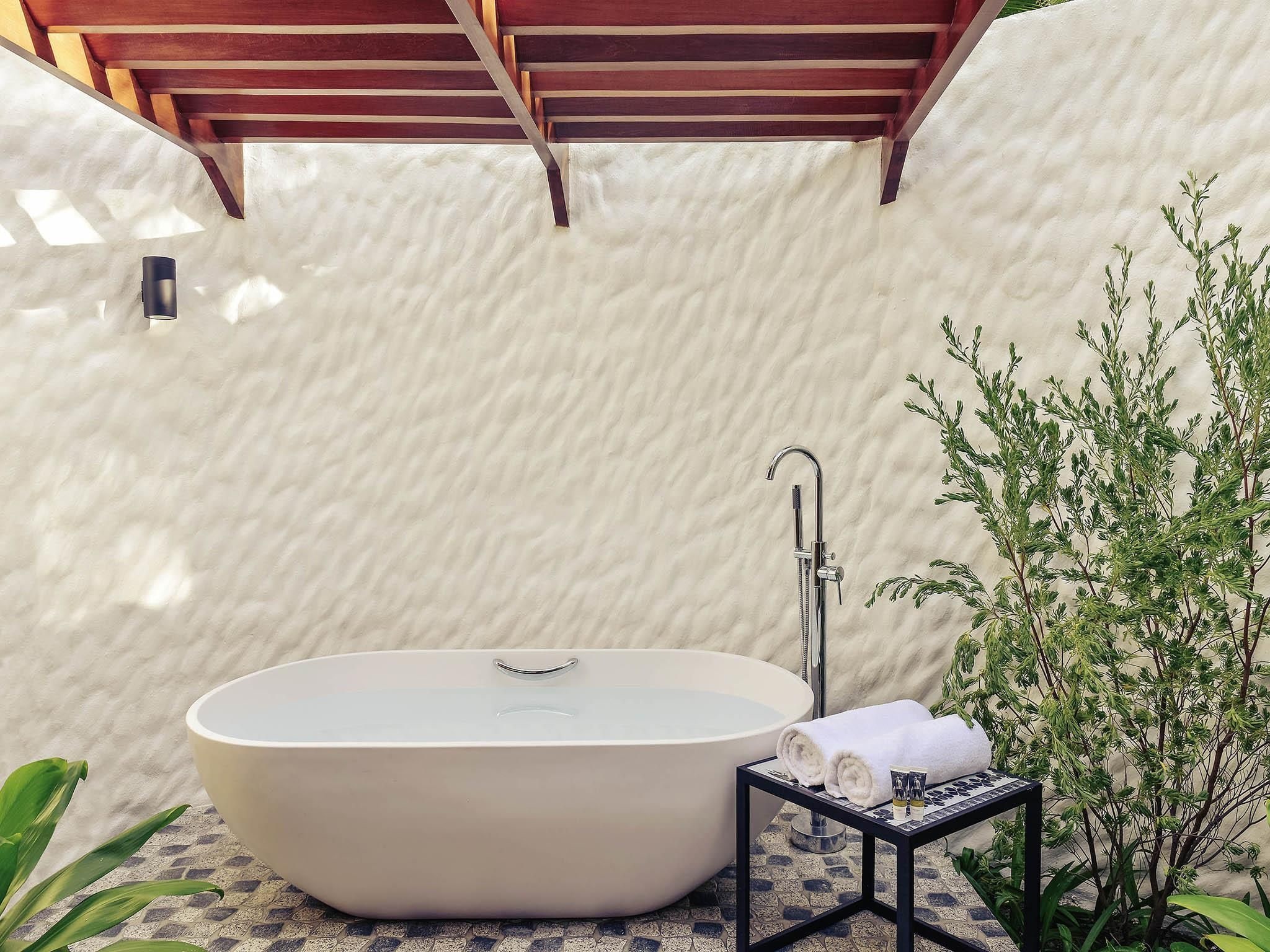 Eine freistehende Badewanne in einem Wellnessbereich, darüber eine Holzhütte und ein kleiner Tisch mit Handtüchern und Zeitschriften.
