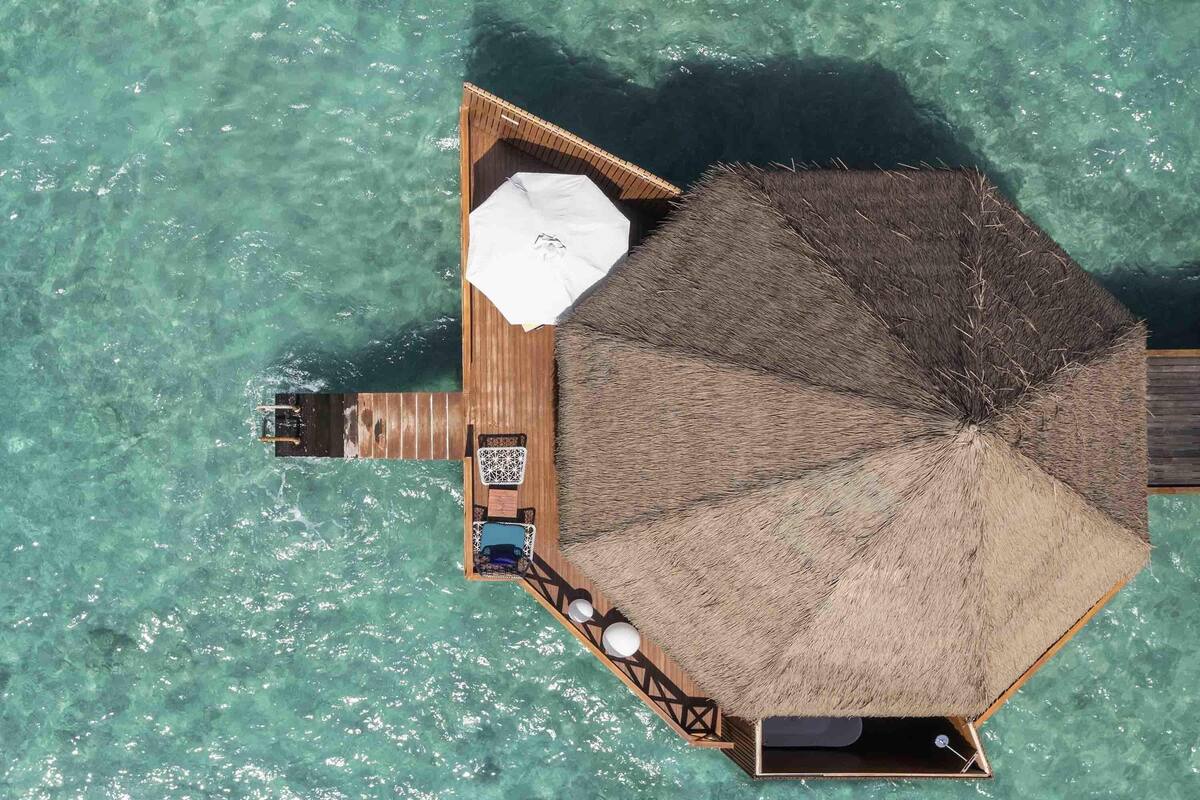 Un bungalow sur pilotis doté d’un toit de chaume, d’une petite terrasse et d’un espace détente avec une table et des chaises.