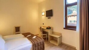 A hotel room with a bed, a desk, a chair, a TV, and a window with curtains. - Europa (Limone sul Garda)