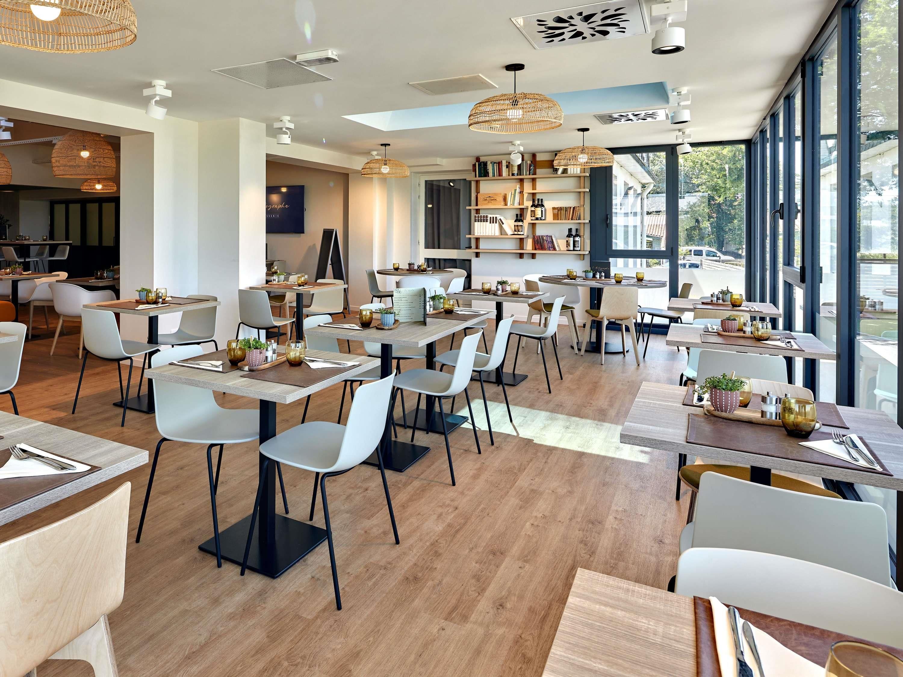 Een modern restaurant met houten tafels, witte stoelen en hangende rotanlampen.