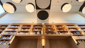 A library with multiple wooden bookshelves and circular ceiling lights. - ibis Styles La Roche-sur-Yon (Mouilleron-le-Captif)