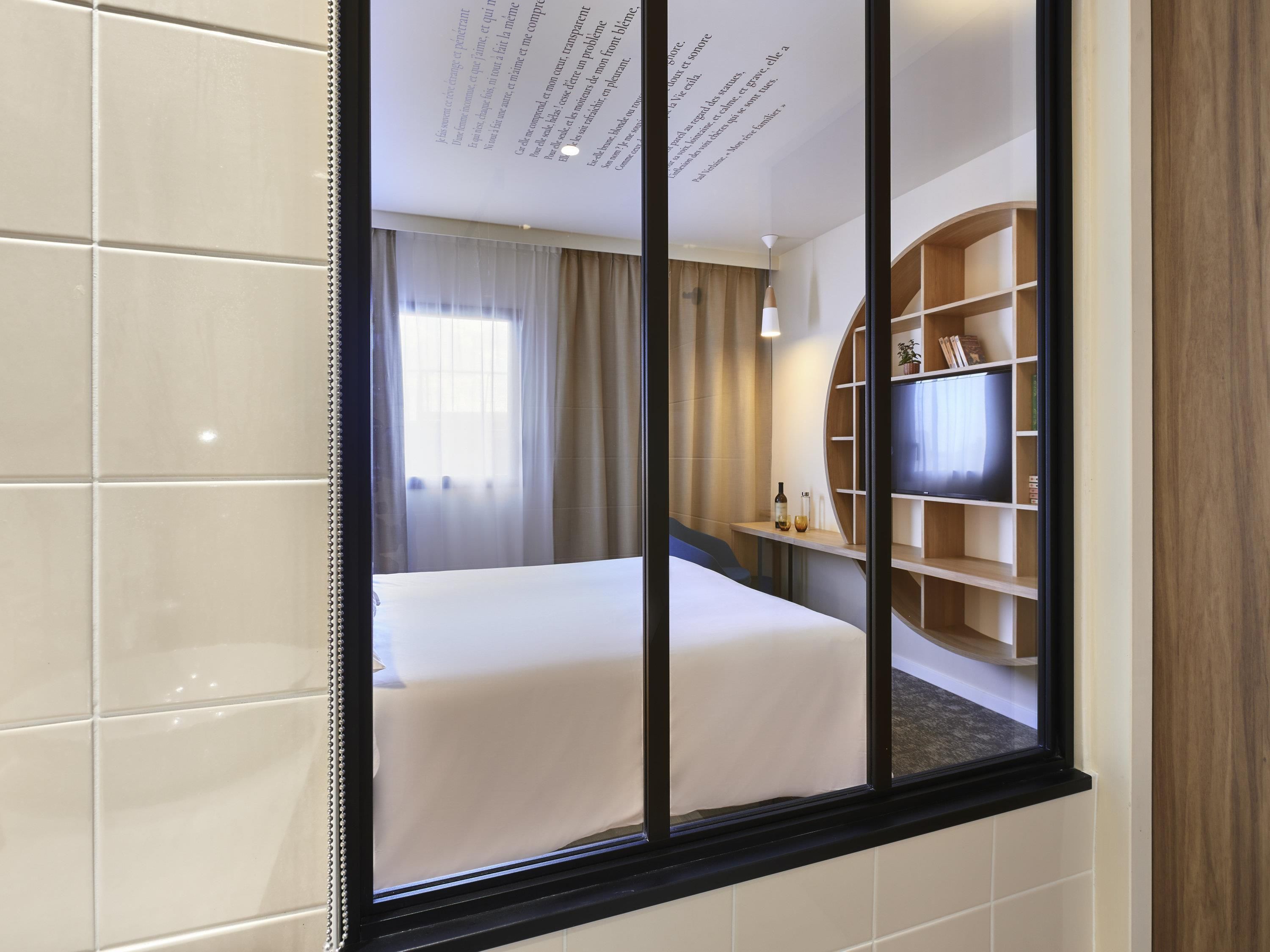 Ein Hotelzimmer mit Bett, Fernseher, Bücherregal und einem Fenster mit Vorhängen.