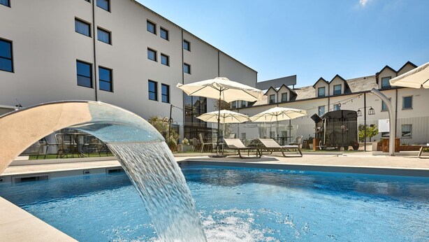 A swimming pool with a water feature, lounge chairs, and umbrellas. - ibis Styles La Roche-sur-Yon (Mouilleron-le-Captif)