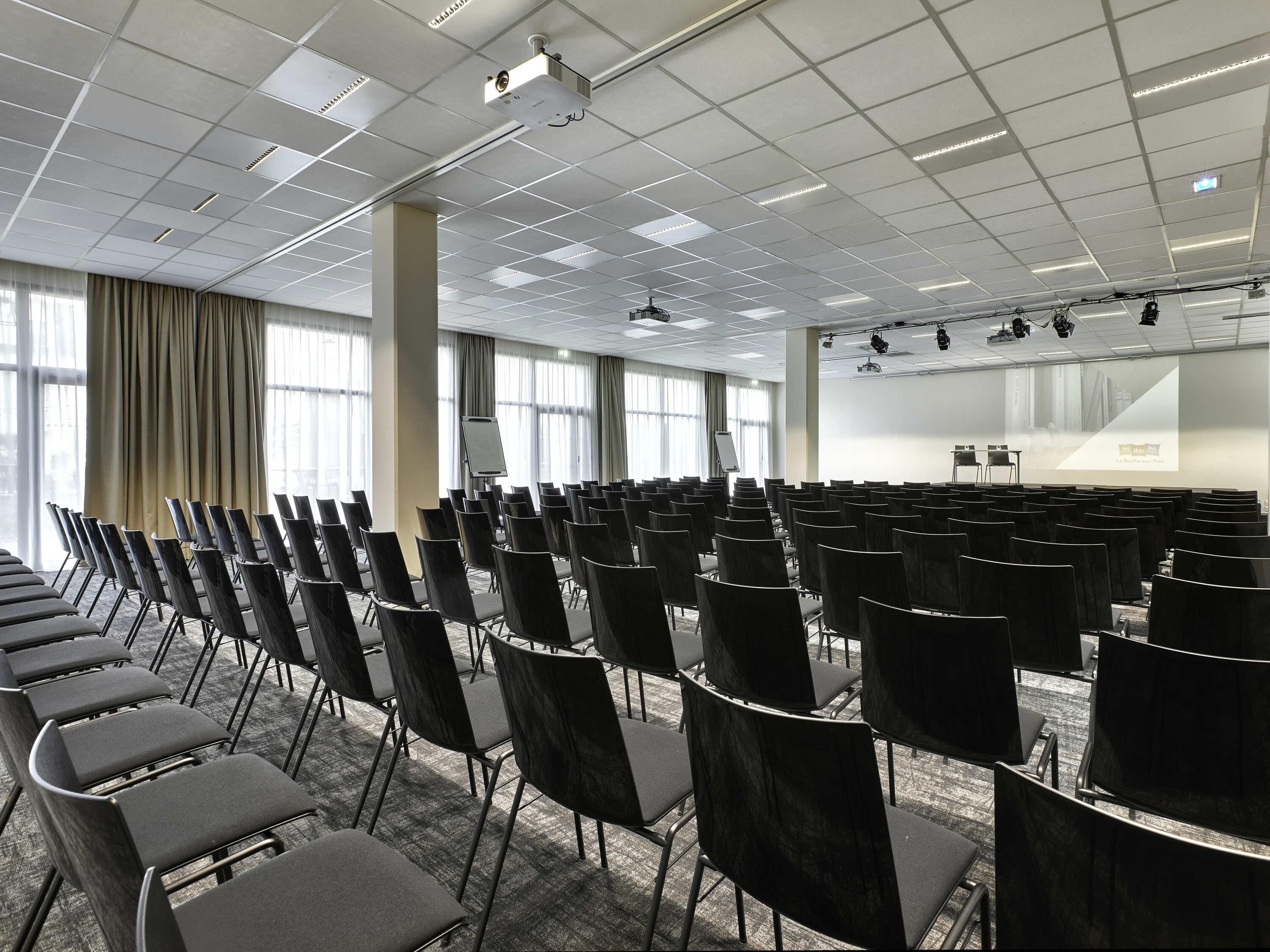 A conference room with rows of chairs, a projector, and a screen.