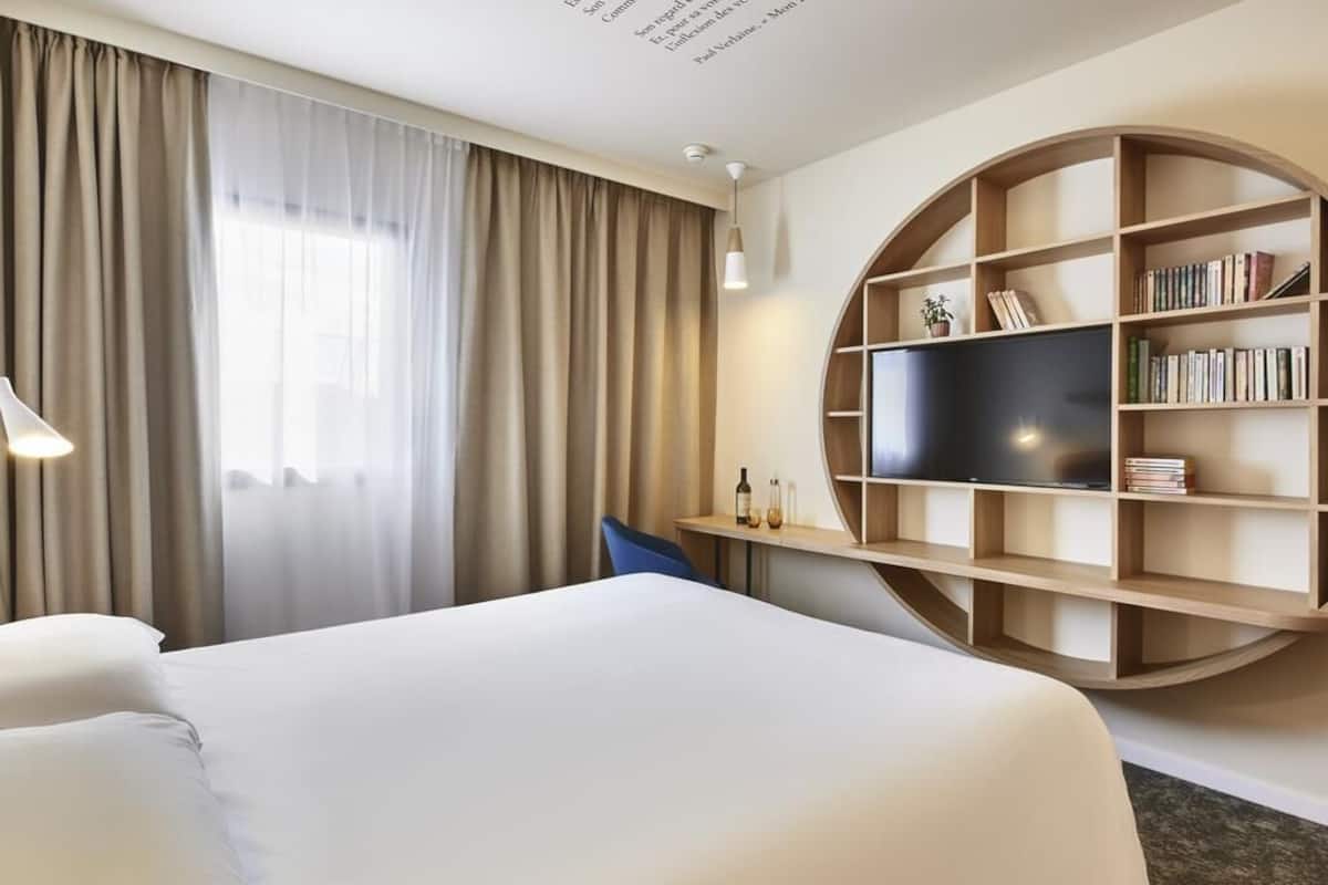 Une chambre d’hôtel avec un lit, une télévision, une bibliothèque et une fenêtre avec des rideaux.