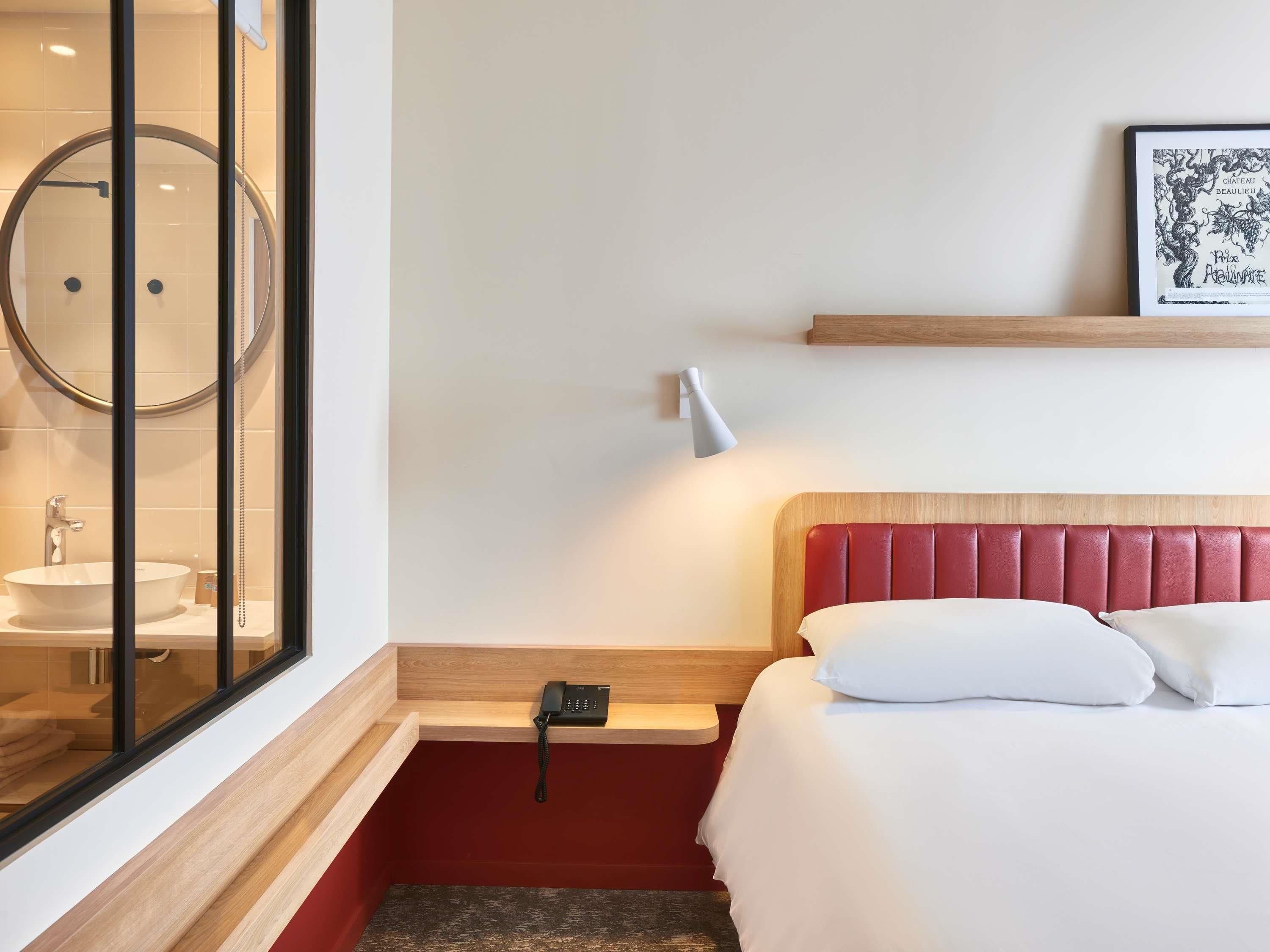 Ein Hotelzimmer mit Bett, Nachttisch, Lampe und einem gerahmten Bild an der Wand.