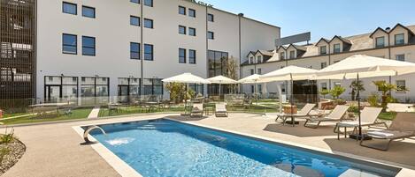 A swimming pool with lounge chairs and umbrellas, surrounded by a building with multiple windows and balconies.