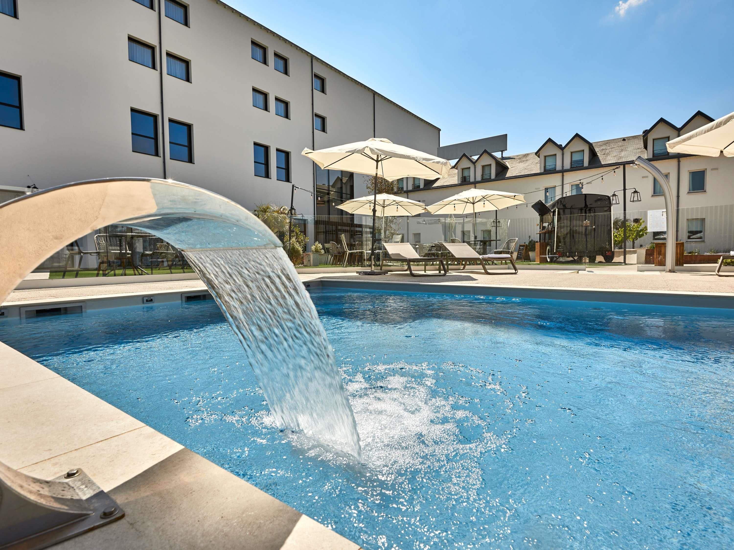 A swimming pool with a water feature, lounge chairs, and umbrellas.