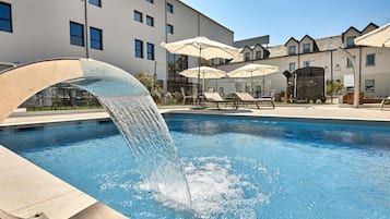 A swimming pool with a water feature, lounge chairs, and umbrellas.