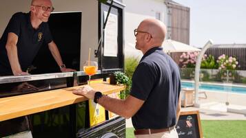 Een foodtruck met een menubord, iemand die eten serveert en een zwembad op de achtergrond.